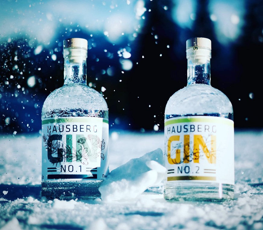 Je eine Flasche Hausberg Gin No.1 und No.2 im Schnee in Garmisch-Partenkirchen am Hausberg. Es schneit auf die Flaschen.