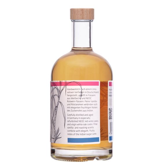 Eine Flasche Hausberg Rum Double Cask 3YO der Edition 3 mit weißem Etikett und Holzgriff-Verschluss in seitlicher Ansicht auf transparentem Hintergrund. Der Inhalt der Flasche erscheint gold-braun.
Auf dem Etikett ist ein Text mit Angaben zur Herstellung und Fasslagerung des Rums.
